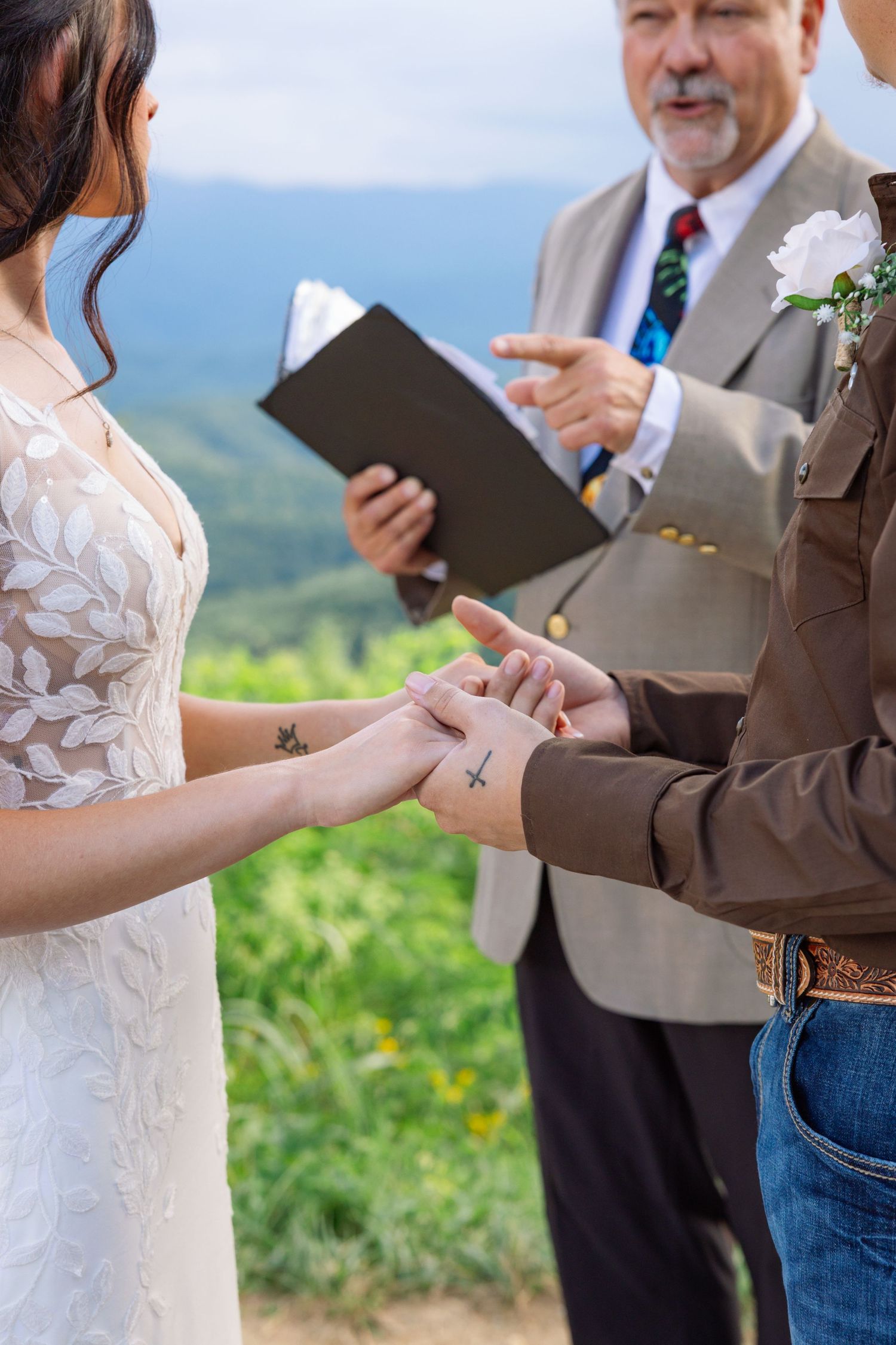 A couple exchanges rings during an outdoor mountain wedding ceremony as an officiant holds a book.