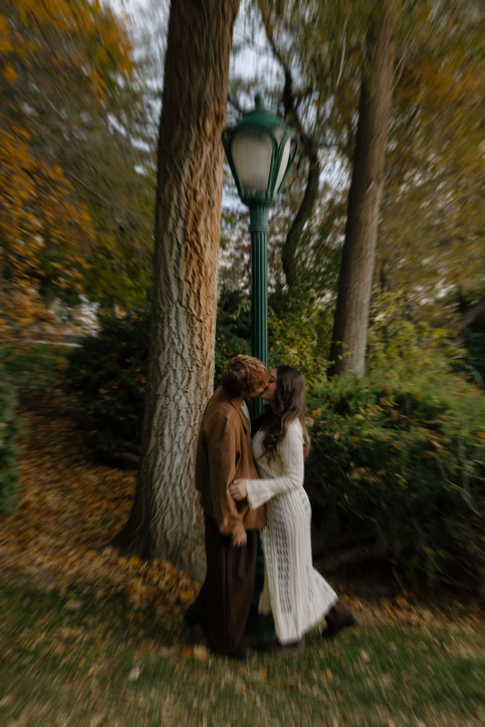 A person in a white dress stands near a large tree trunk in an autumn forest setting with blurred motion effects.