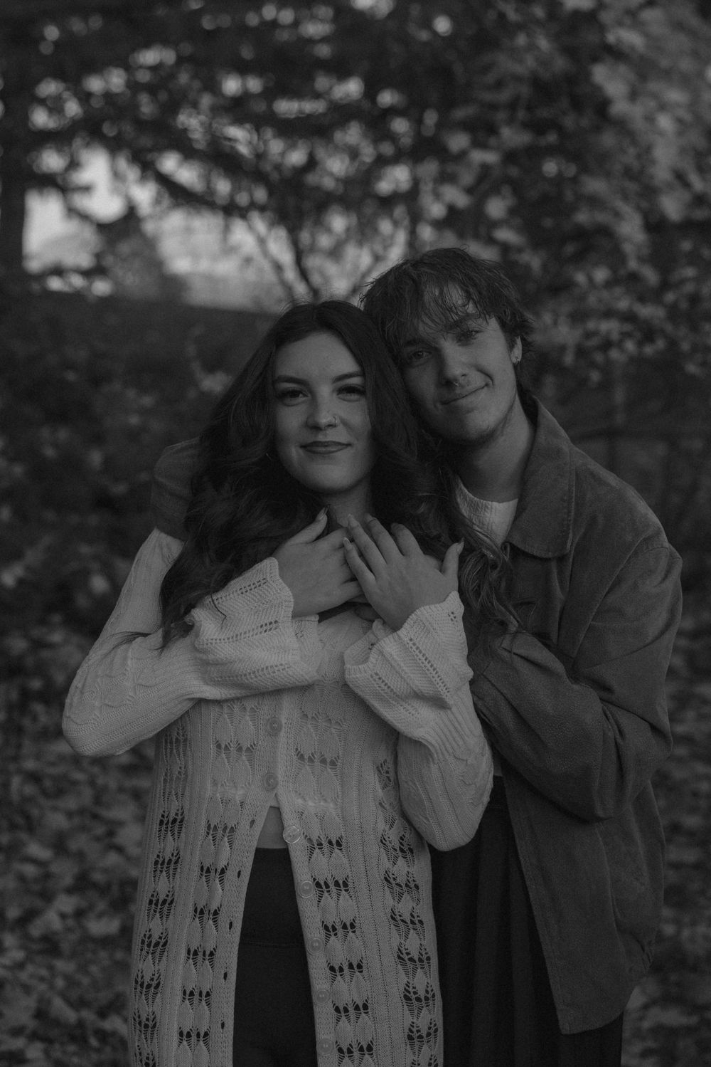 Black and white romantic photo series showing a couple embracing outdoors among trees in a natural setting.