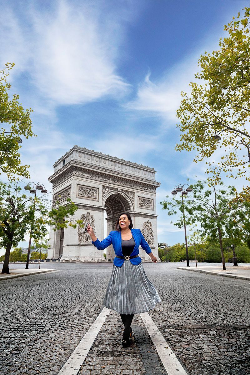 Tourist poses on cobblestone street with the iconic Arc de Triomphe monument in Paris, France.