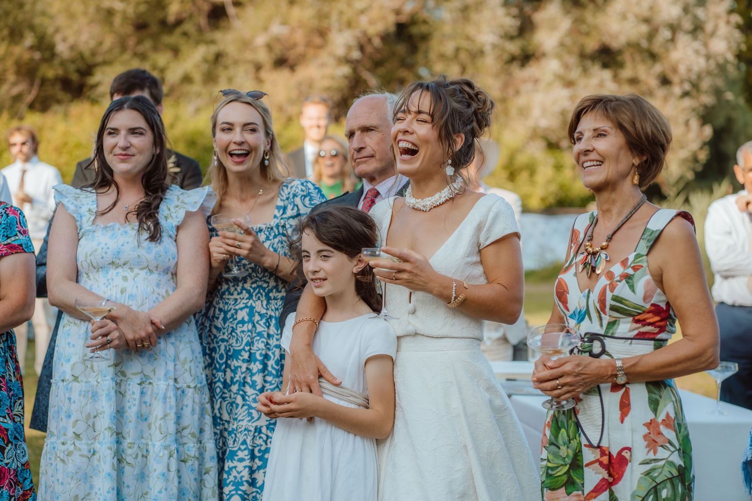 A group of guests in summer dresses share a joyful moment during an outdoor celebration.