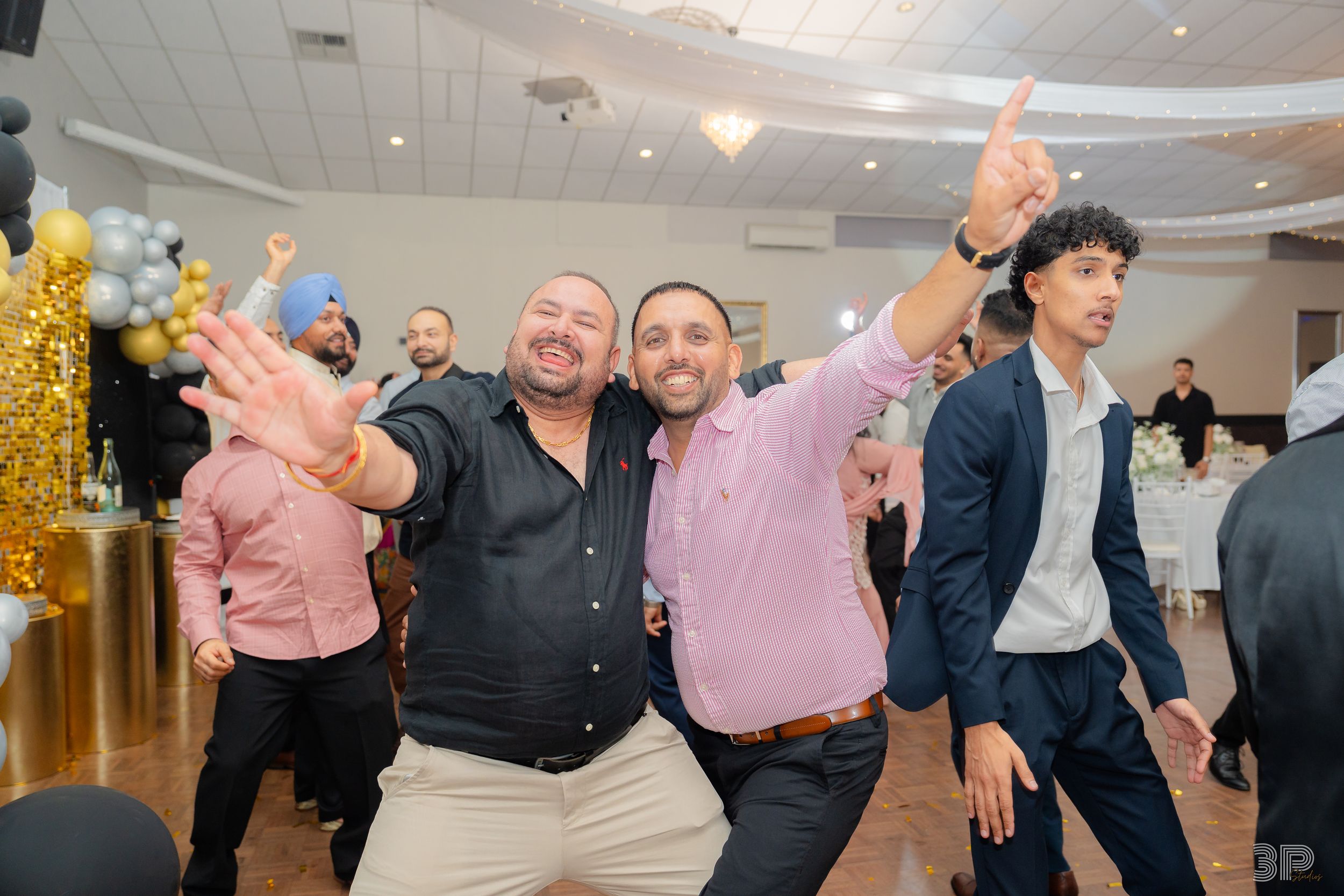 A lively group of people dancing together at a formal event in a brightly lit banquet hall.