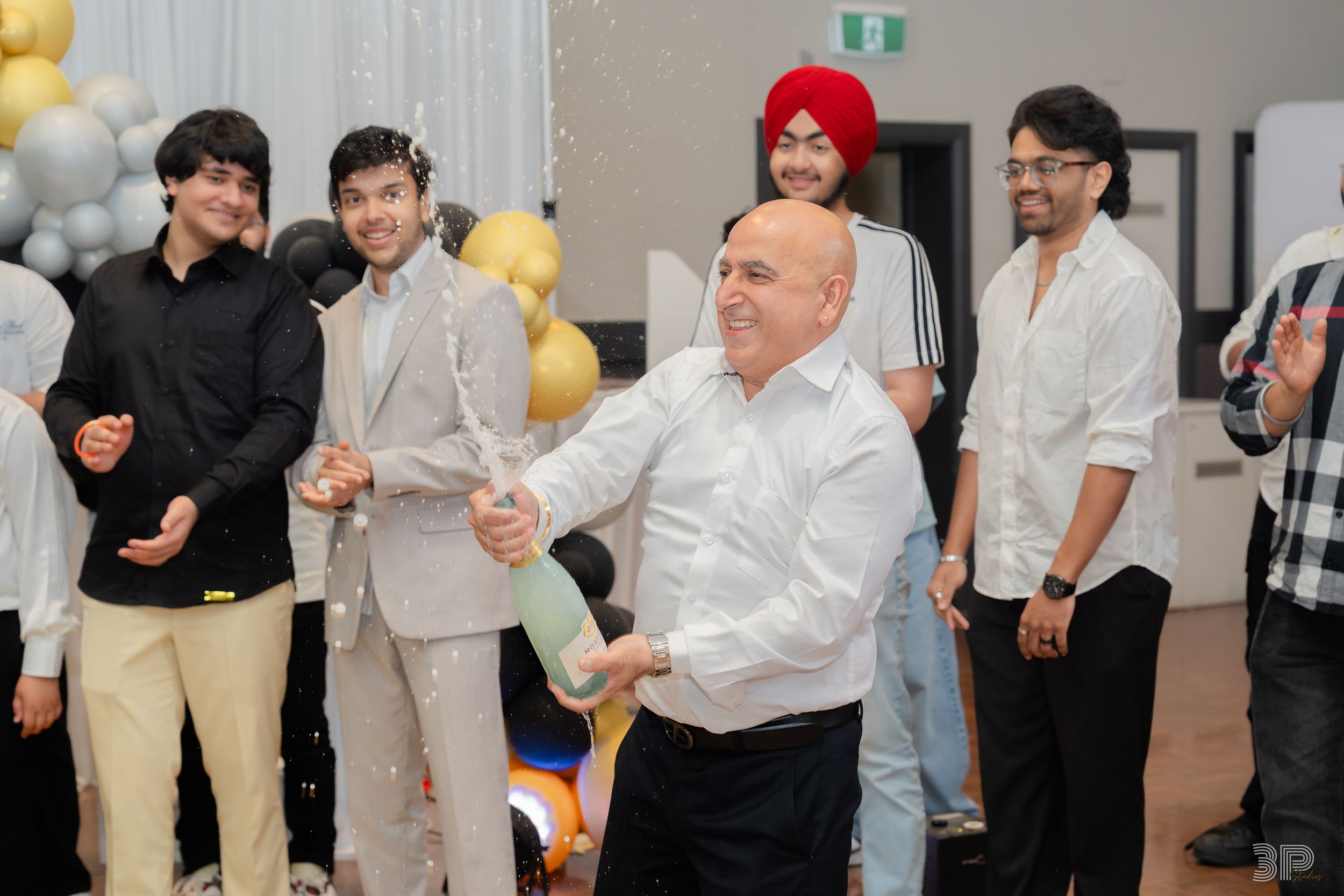 People in white and black attire gather at a social event with yellow balloons in the background.