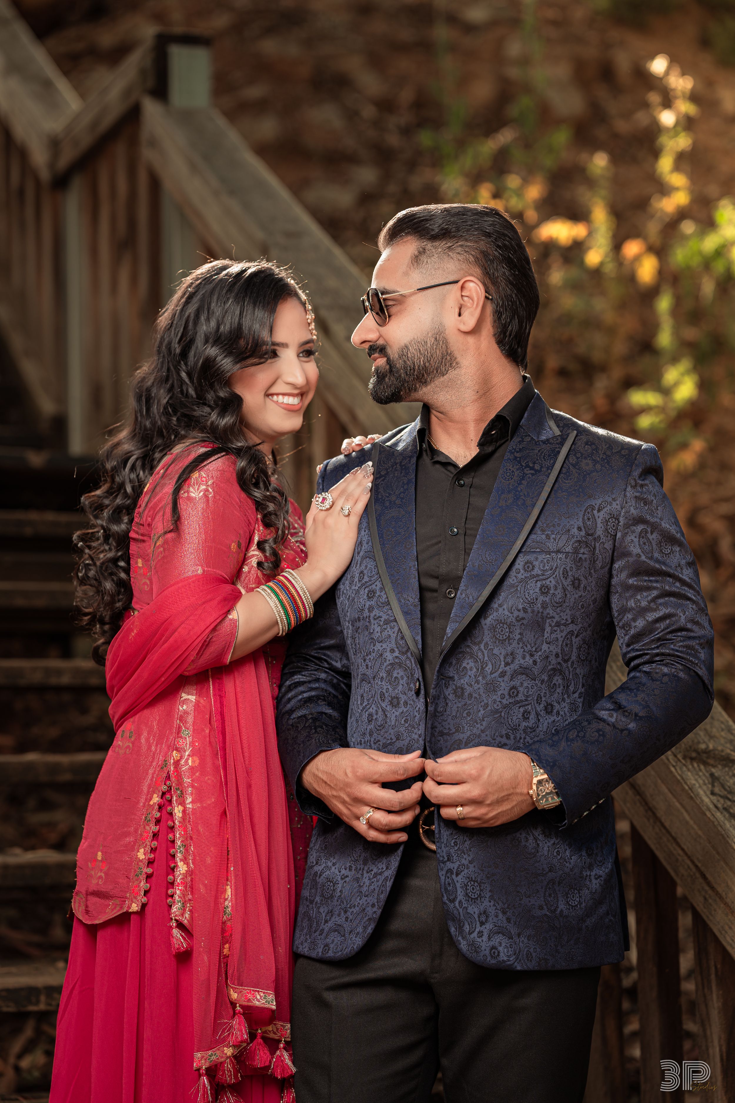 A romantic couple in formal attire shares intimate moments outdoors, with the woman wearing a red traditional dress.