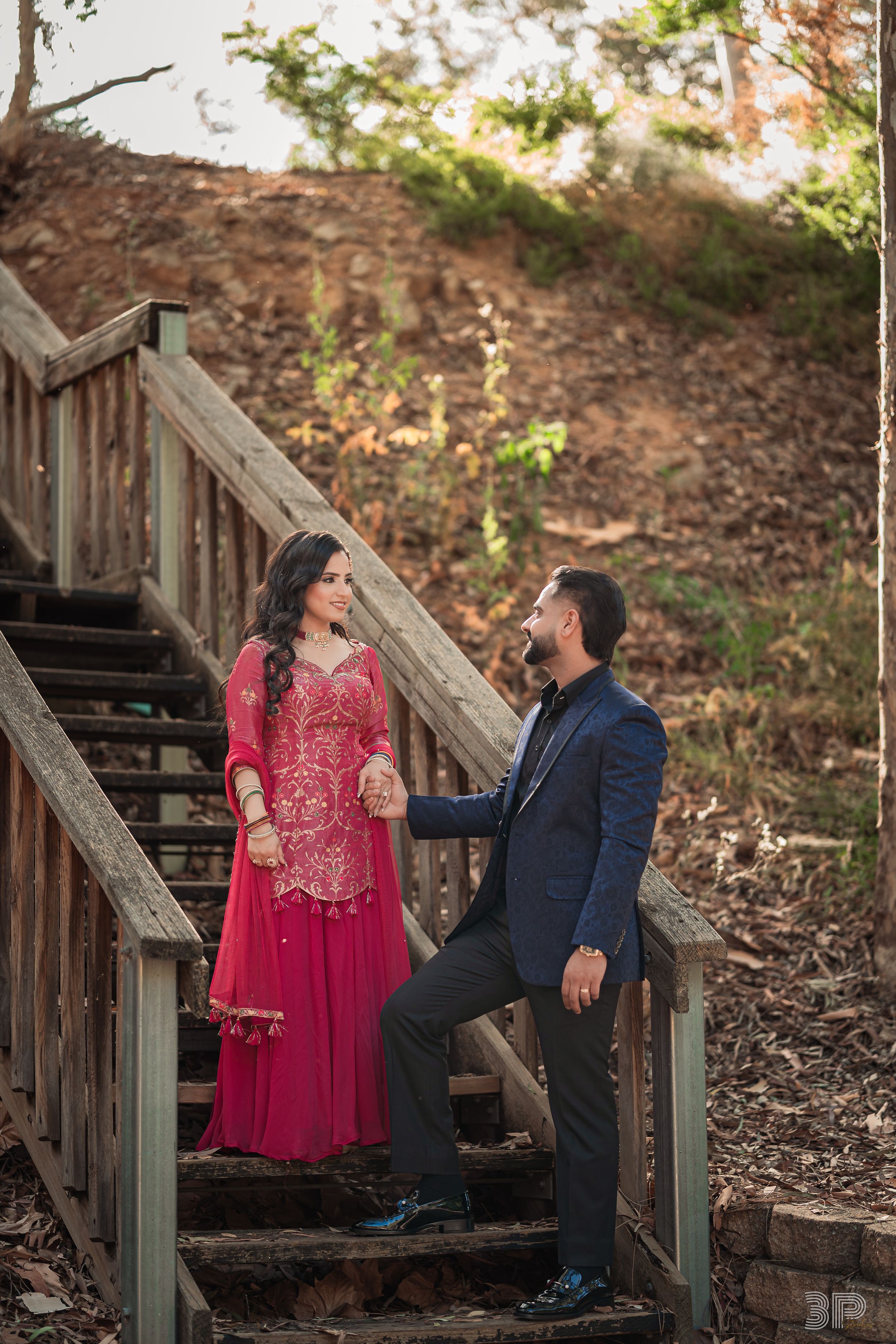 Couple in red dress and navy suit share romantic moments on wooden stairs in an outdoor autumn setting.