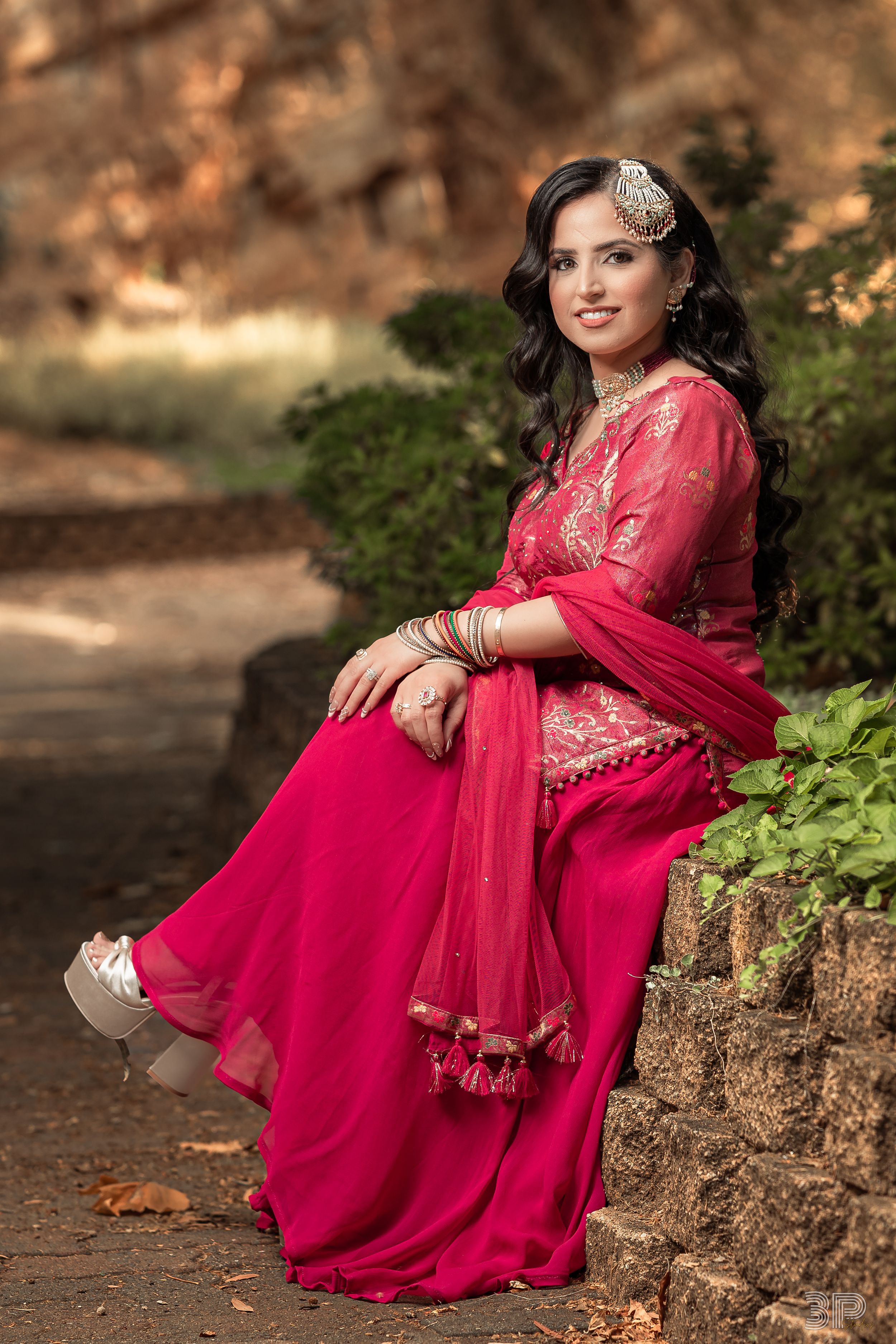 A woman in a vibrant red traditional dress poses gracefully on stone steps surrounded by autumn foliage.