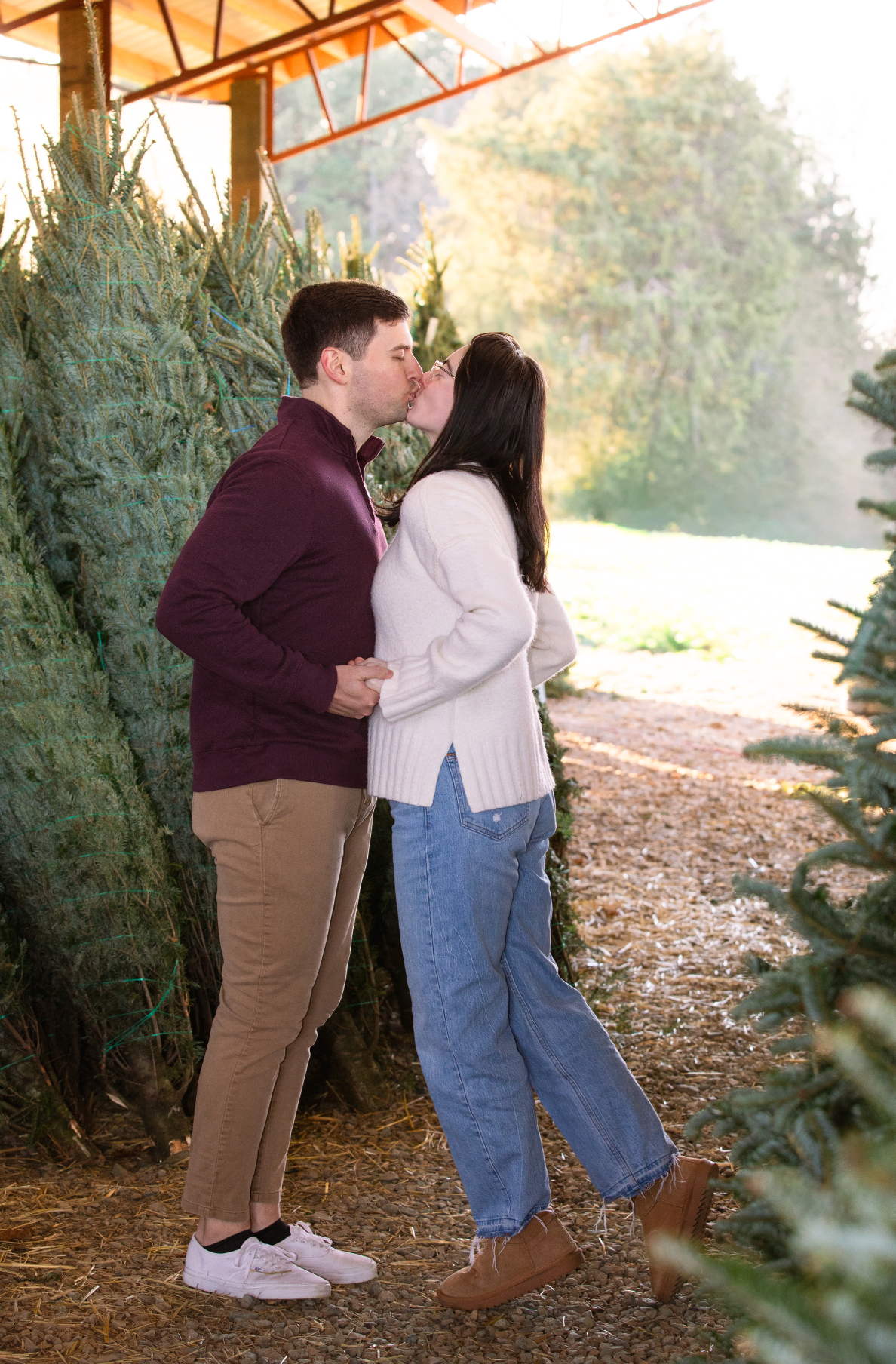 A couple shares a romantic moment among evergreen trees at a Christmas tree Farm