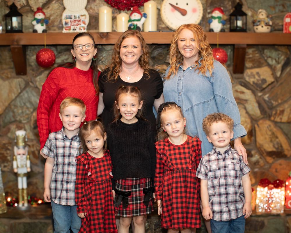A group in coordinating red plaid and black outfits poses together for a holiday photo in front of a stone fireplace.
