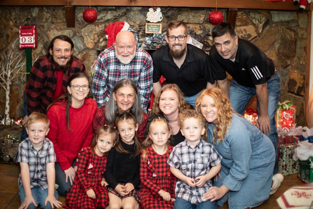 A family group wearing coordinated red and black buffalo plaid outfits poses together for a holiday portrait.