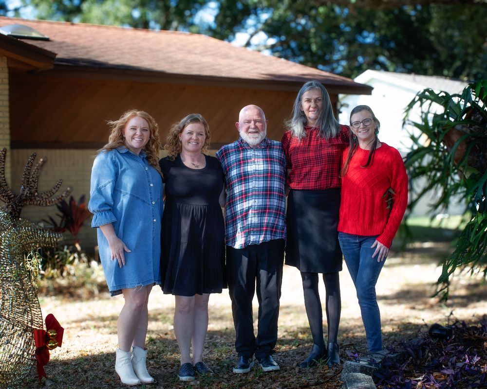 Family group in coordinated outfits poses outdoors on a sunny day among trees and natural scenery.