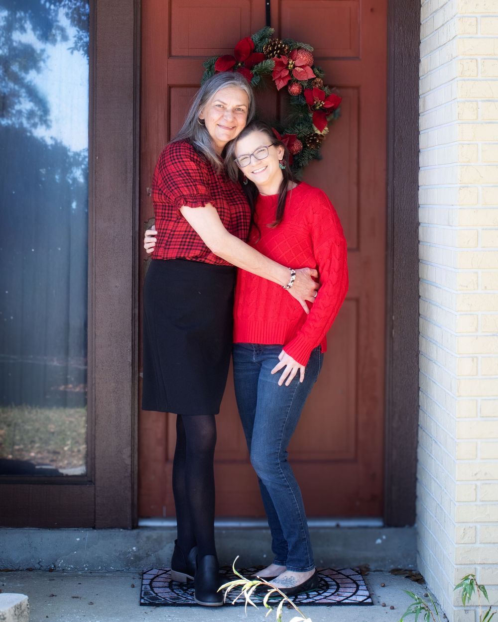 Family members pose in coordinated red and black outfits against a brown door and brick wall.