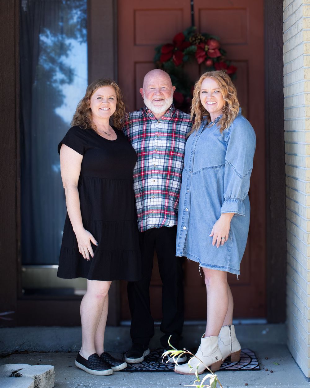 Family group portrait on a porch with coordinated outfits in front of a brown door.