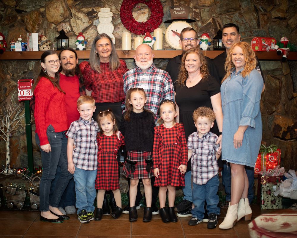 Family group wearing coordinated red and black plaid outfits poses for holiday photos in front of Christmas decorations.