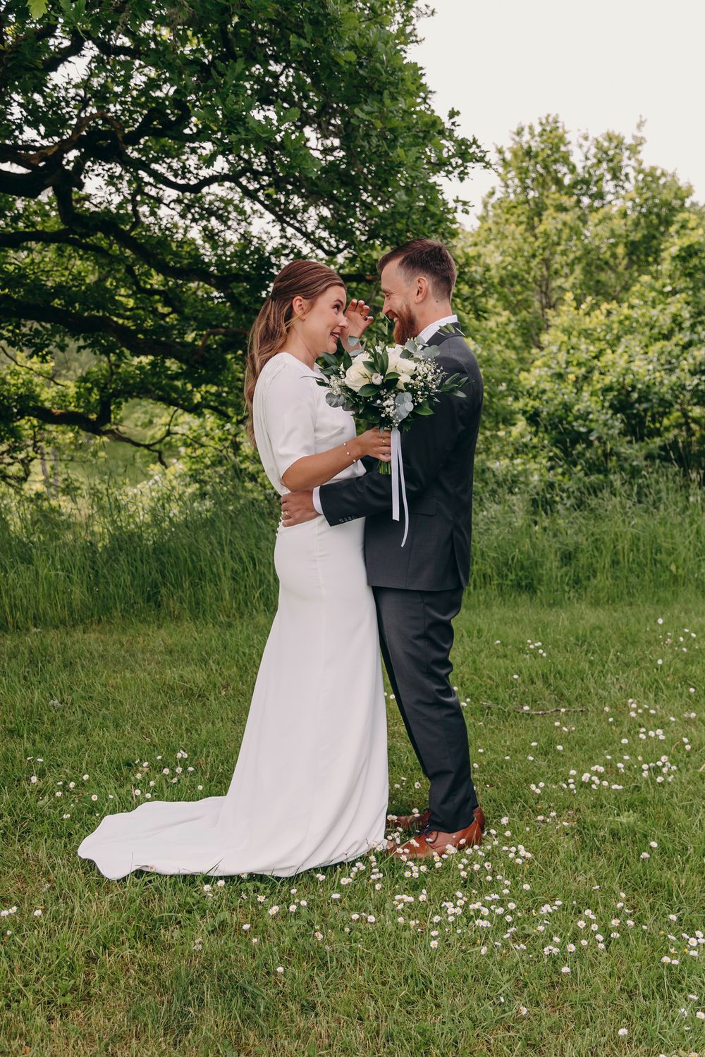 A couple shares a romantic moment in a lush green meadow during their outdoor wedding photoshoot.