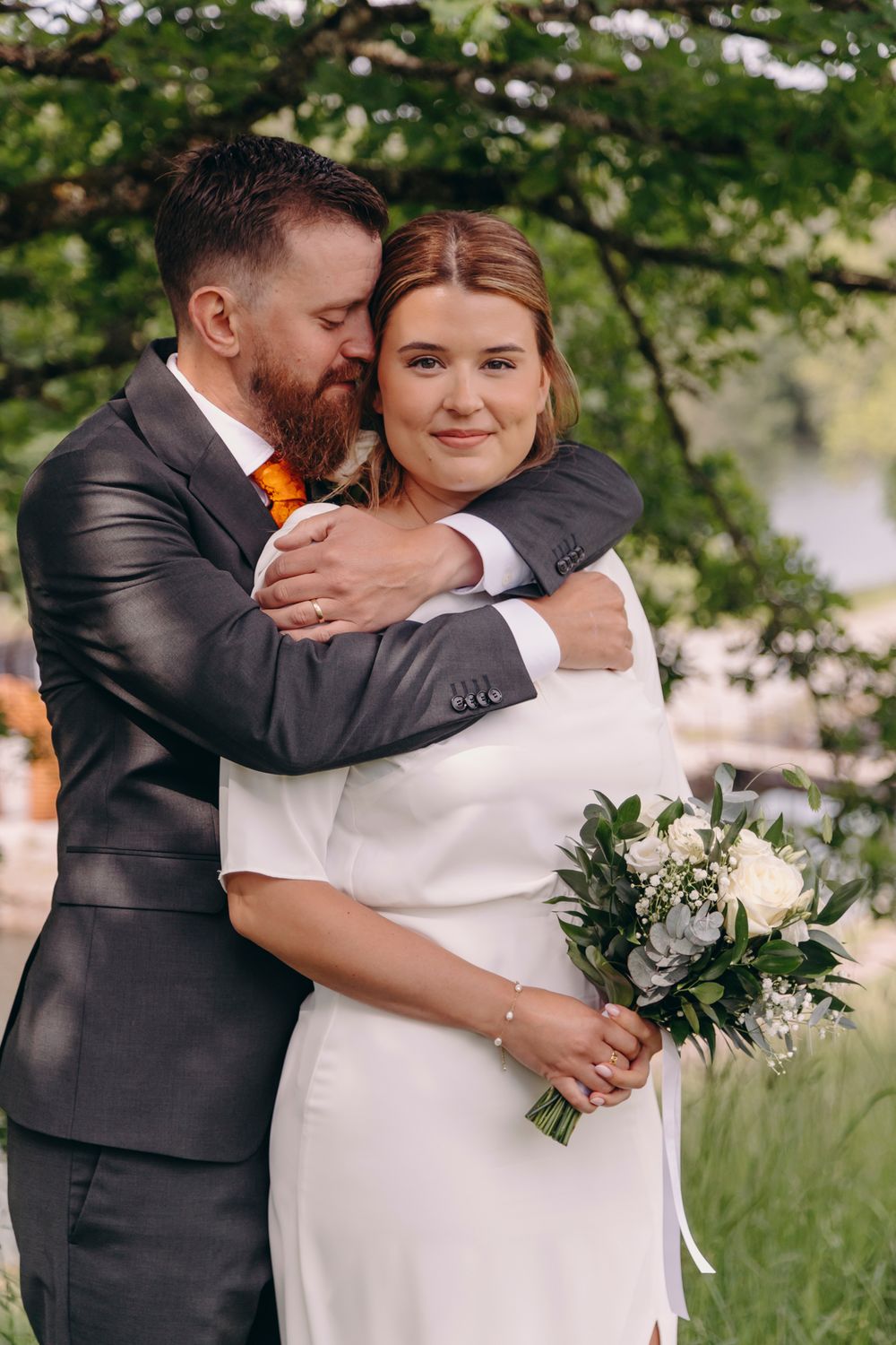 Romantic wedding couple embraces outdoors in a natural garden setting with soft greenery in the background.