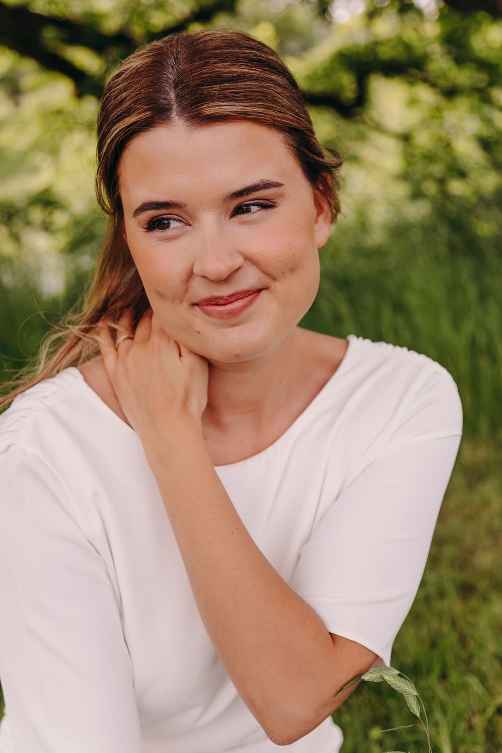 A person in a white t-shirt sits outdoors smiling and laughing while covering their mouth in a series of candid shots.
