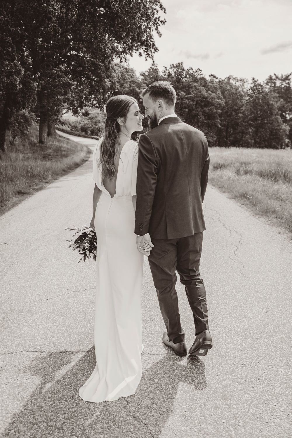 A bride and groom walk down a country road together in a series of romantic black and white photos.