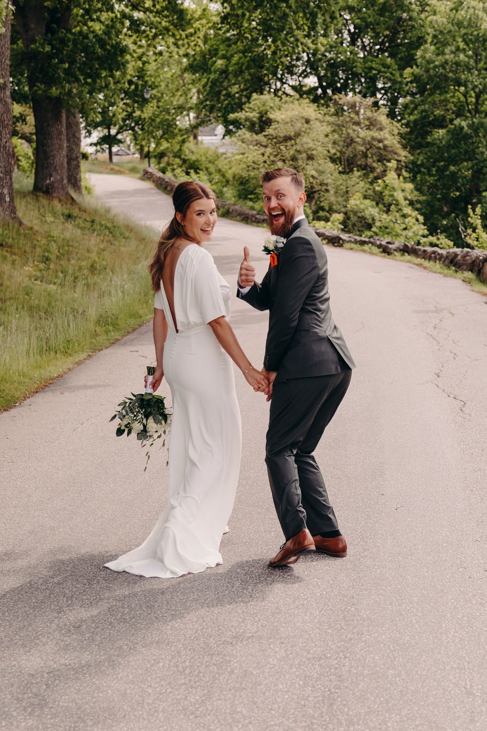 A couple in wedding attire shares a playful moment on a tree-lined path during their wedding photoshoot.