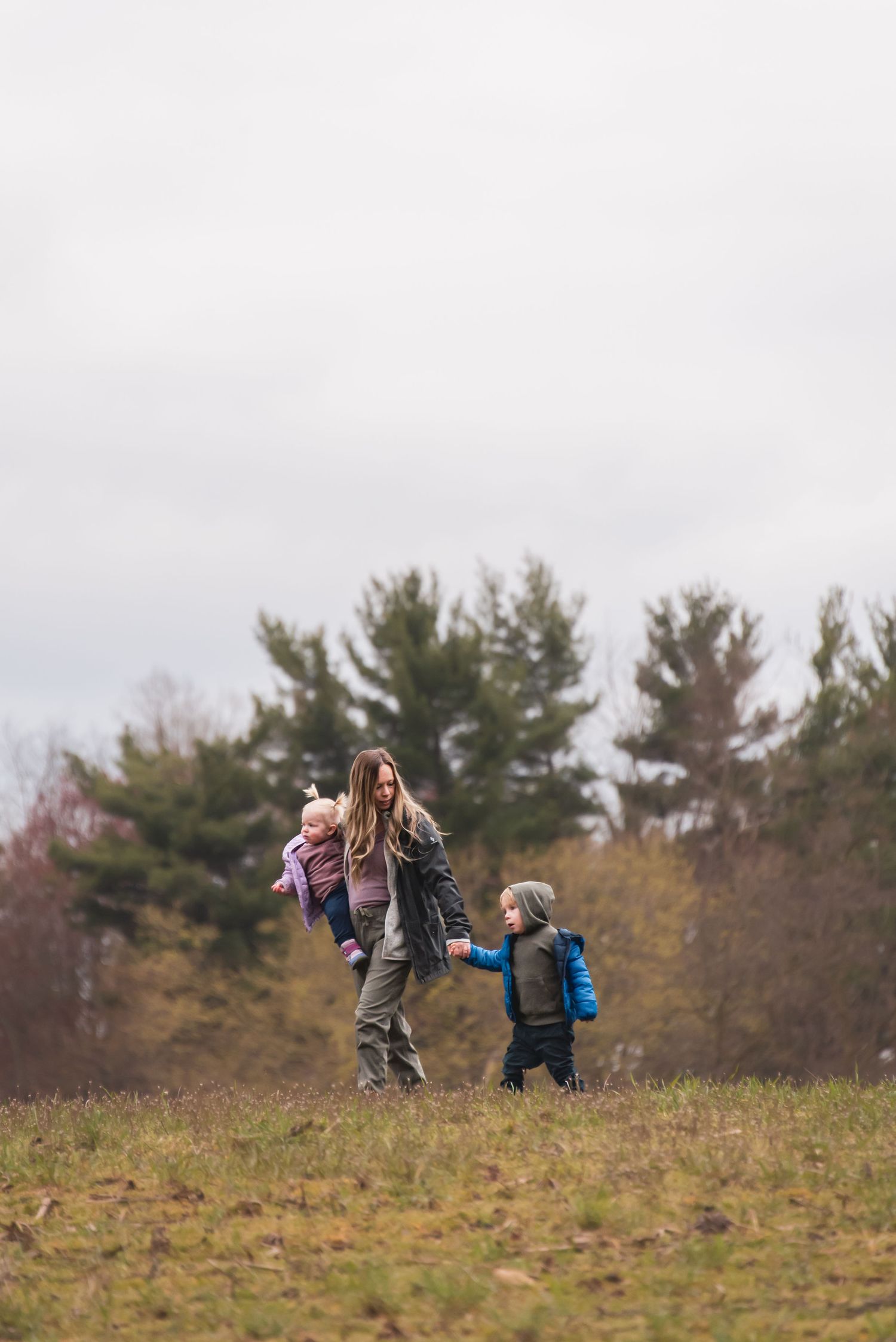 People walking up a grassy hill carrying backpacks on an overcast day.