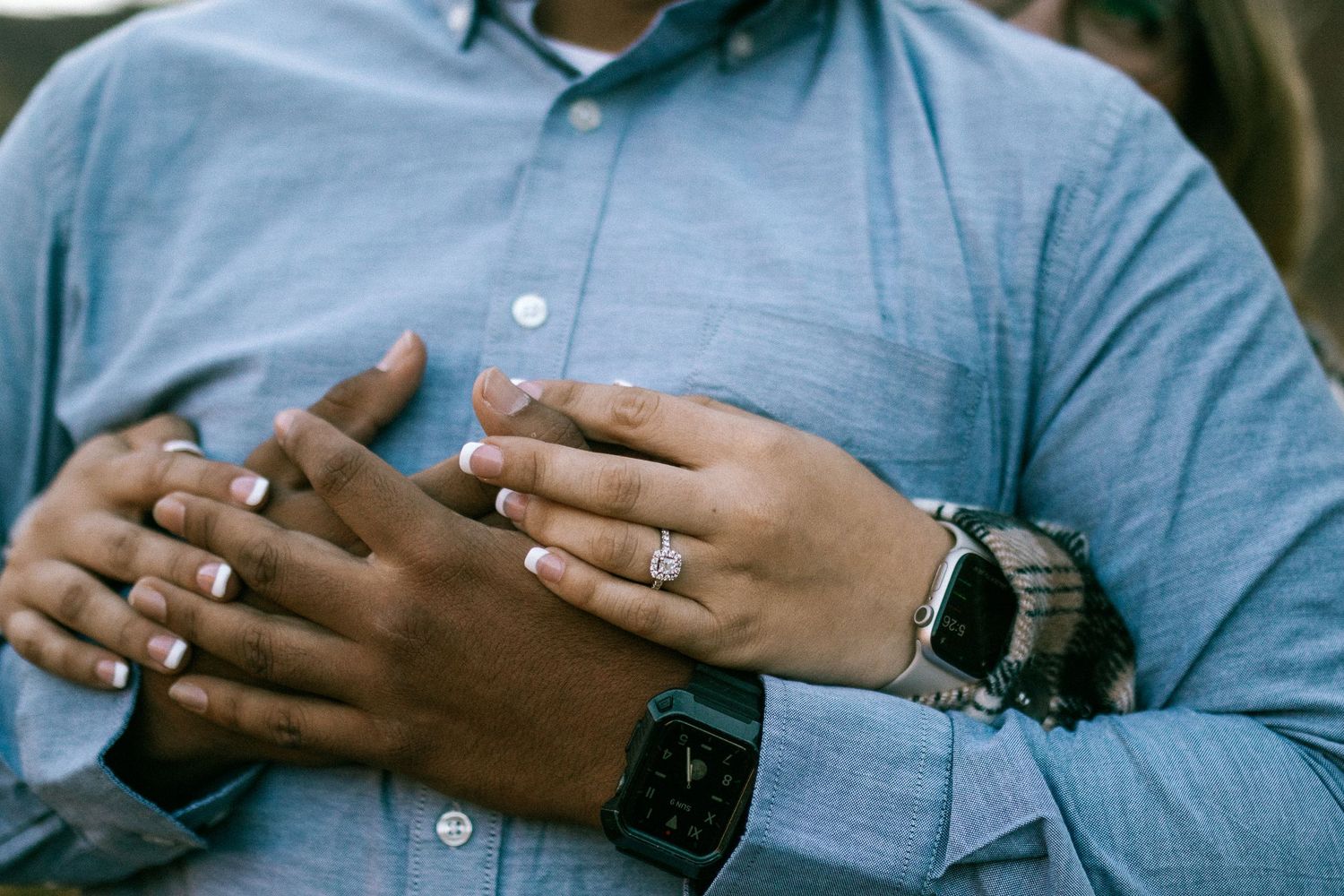 Close-up of hands wearing rings and a smartwatch against a light blue shirt.