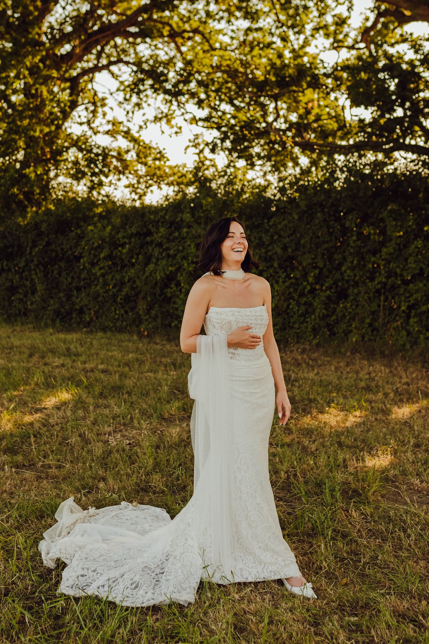 Bride standing alone in a field during golden hour, holding her bouquet.