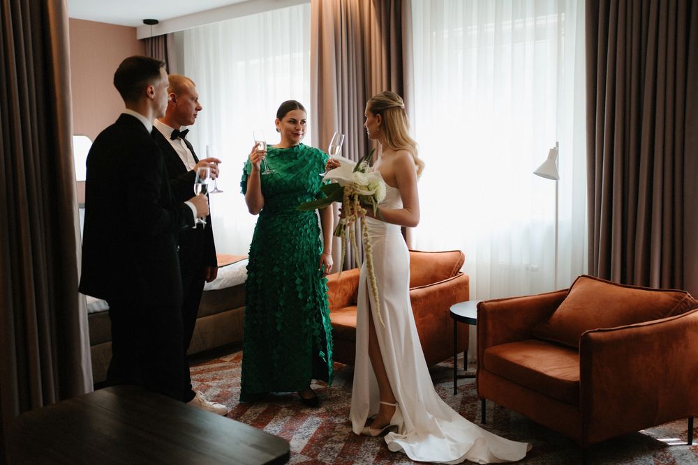 Wedding preparation scene in hotel room with guests in elegant attire.