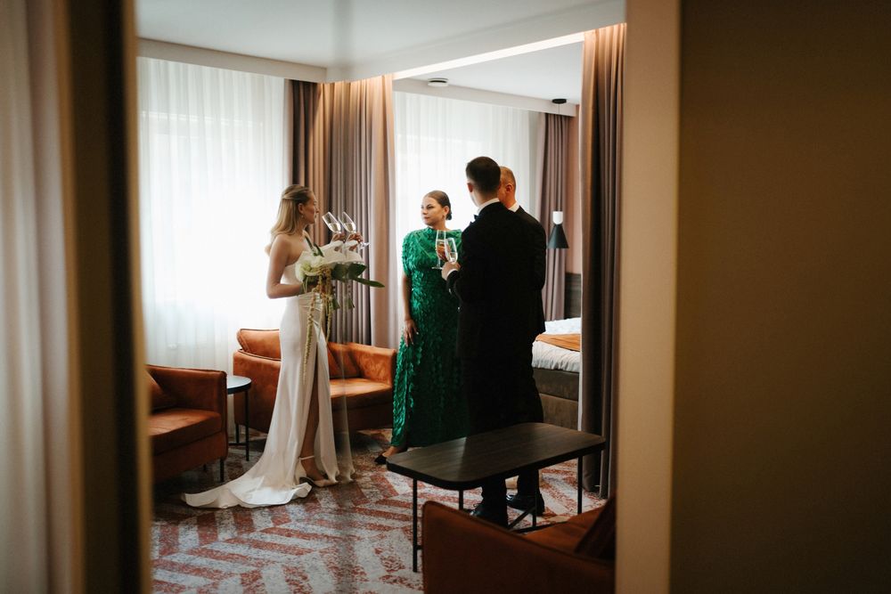 Wedding party gathering in hotel room reflected through doorway mirror.