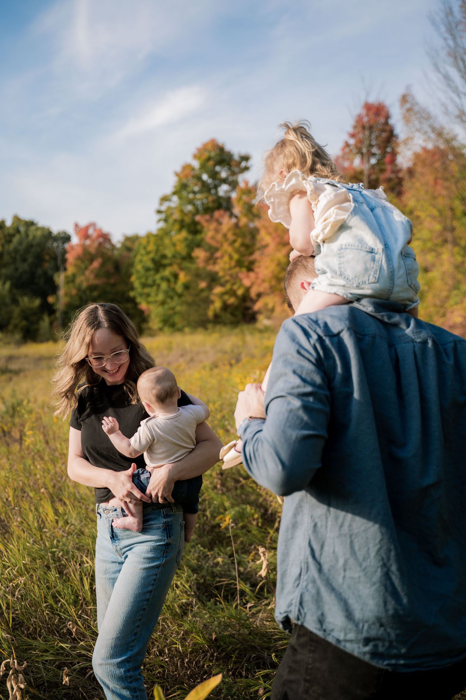 A couple shares intimate moments in a sunny autumn field with golden grass and colorful fall foliage in the background.