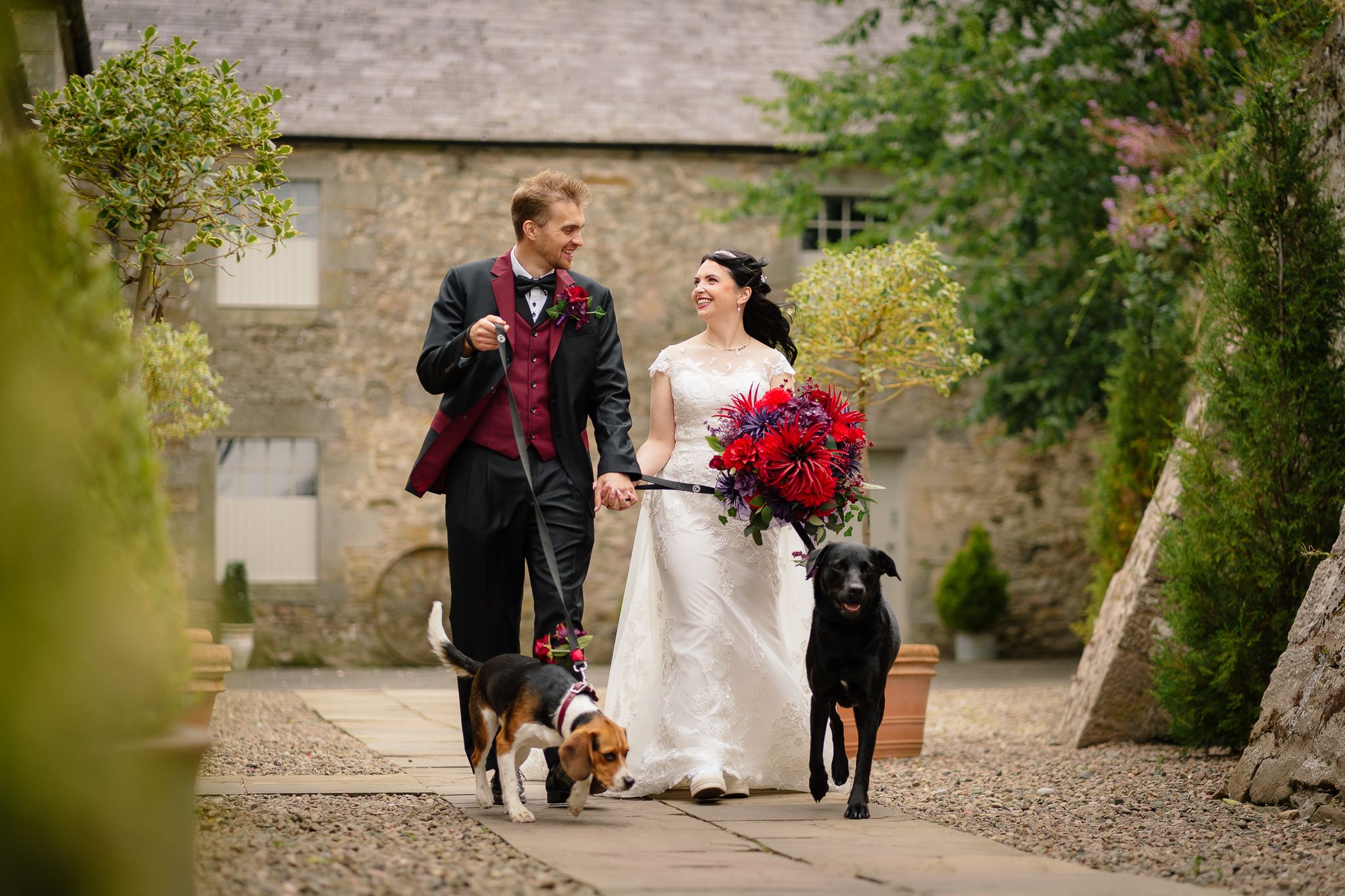 Wedding party walking through a garden path with stone walls and greenery. Doxford Barns