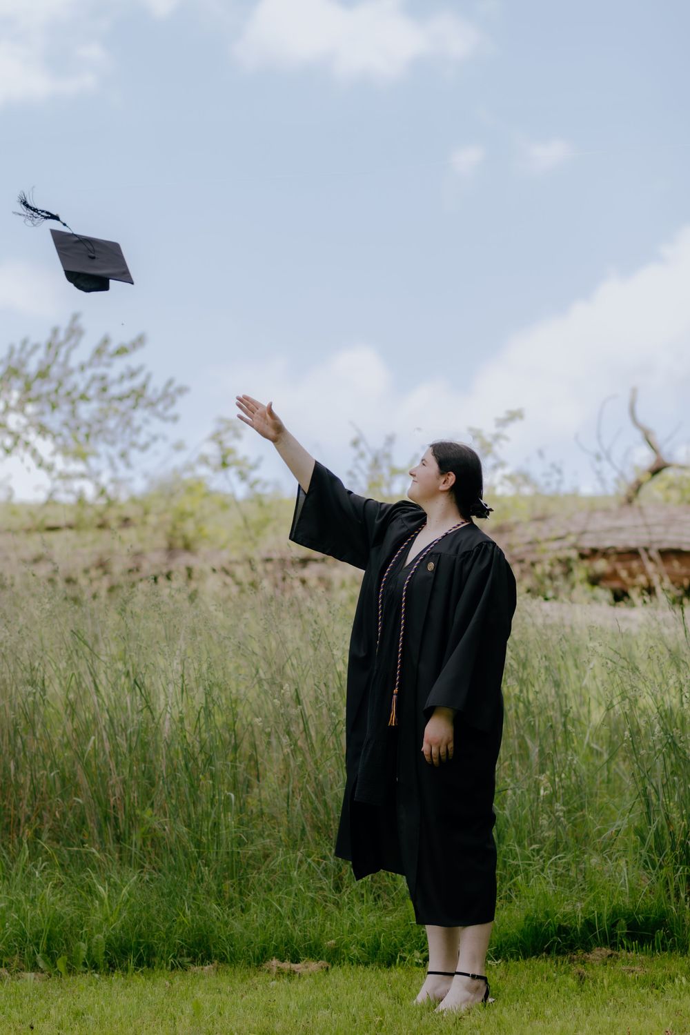 Graduate throwing mortarboard cap into blue sky during graduation celebration.