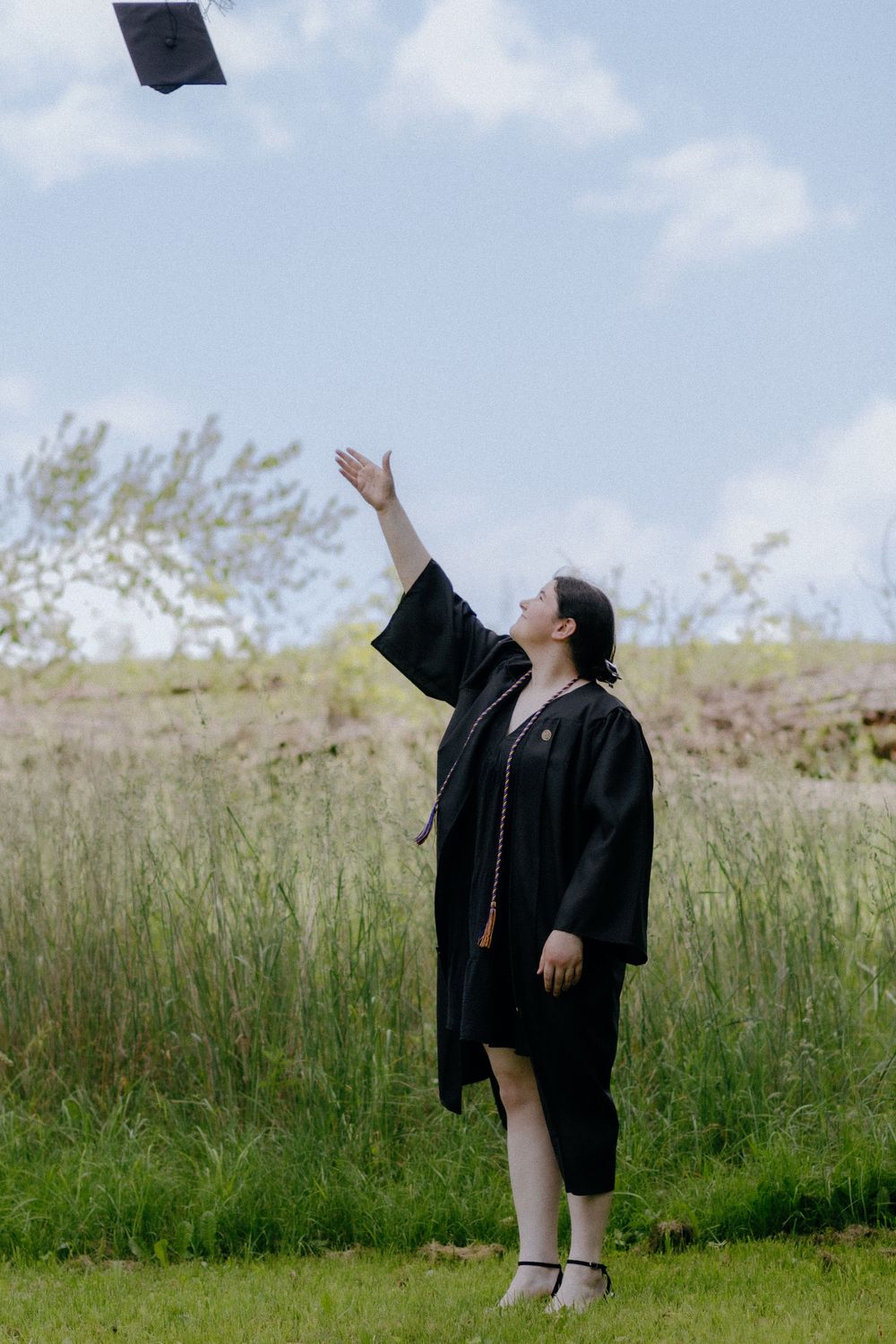 Graduate making peace sign while celebrating in cap and gown outdoors.