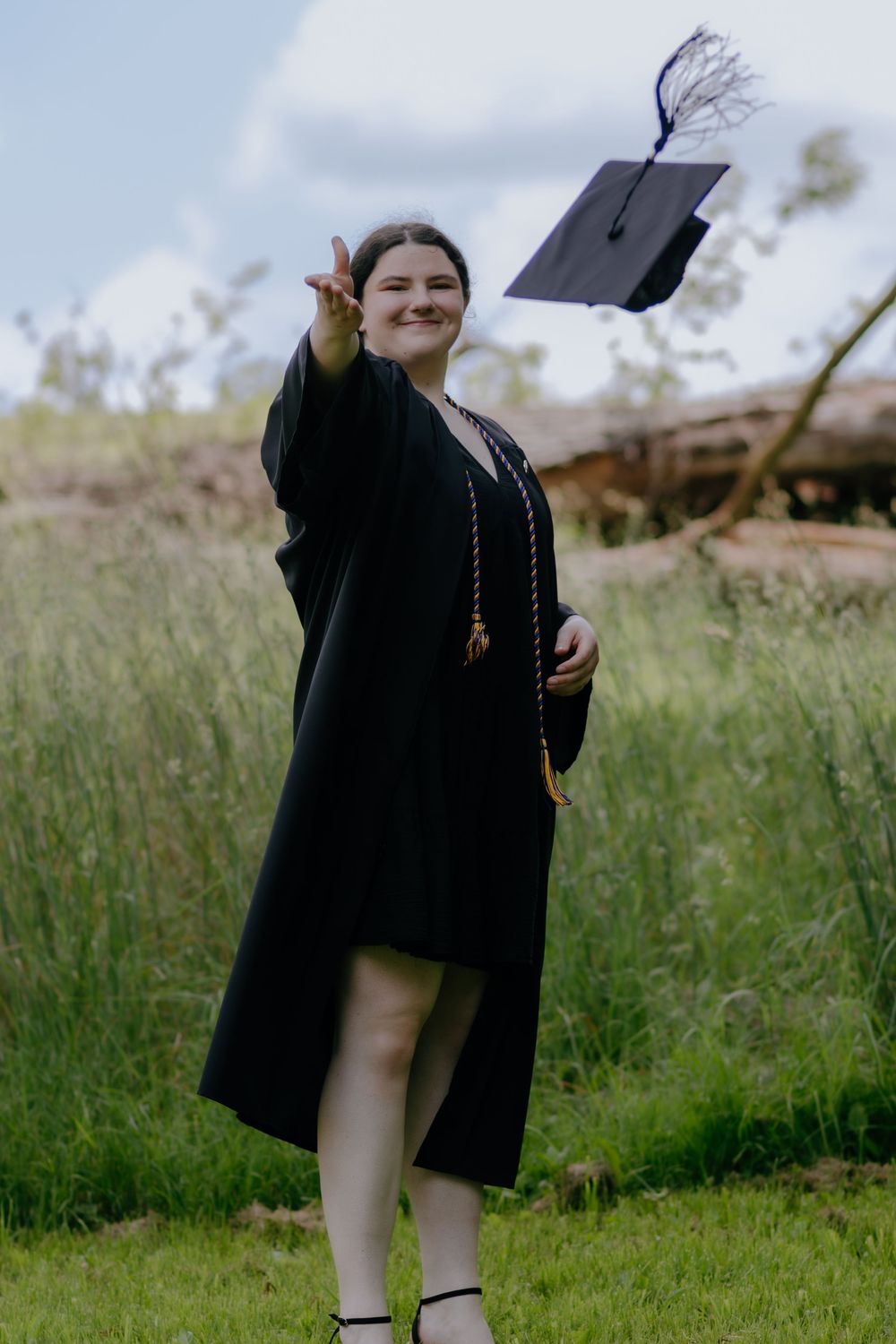 Graduate tossing cap in celebration while standing in grassy field.