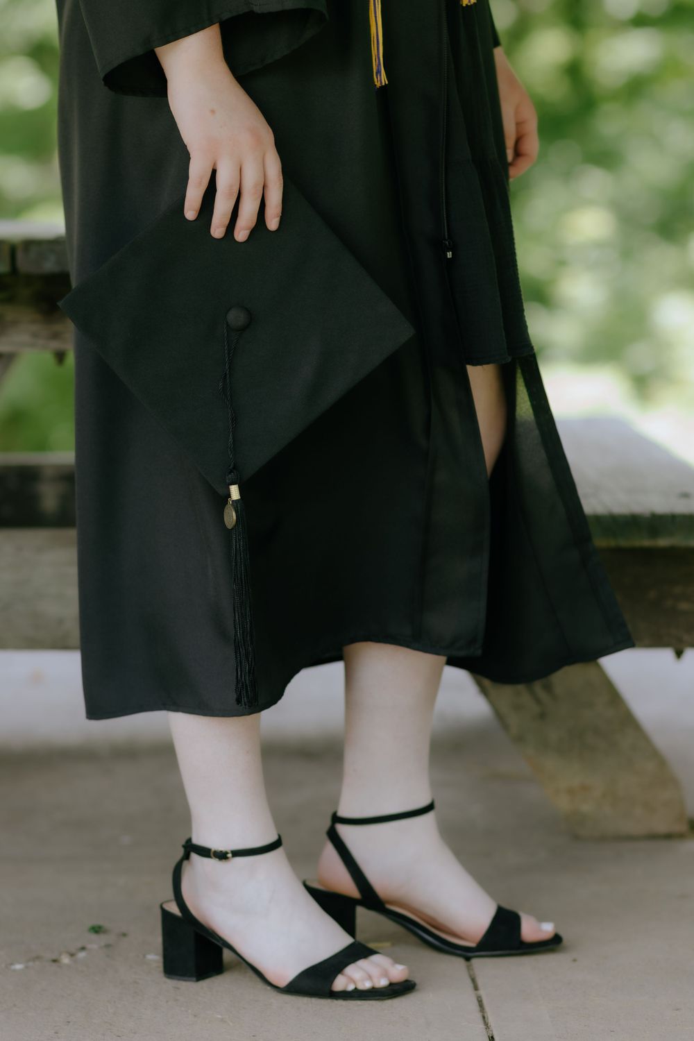 Close-up of graduation gown and cap with black sandals and tassel detail.