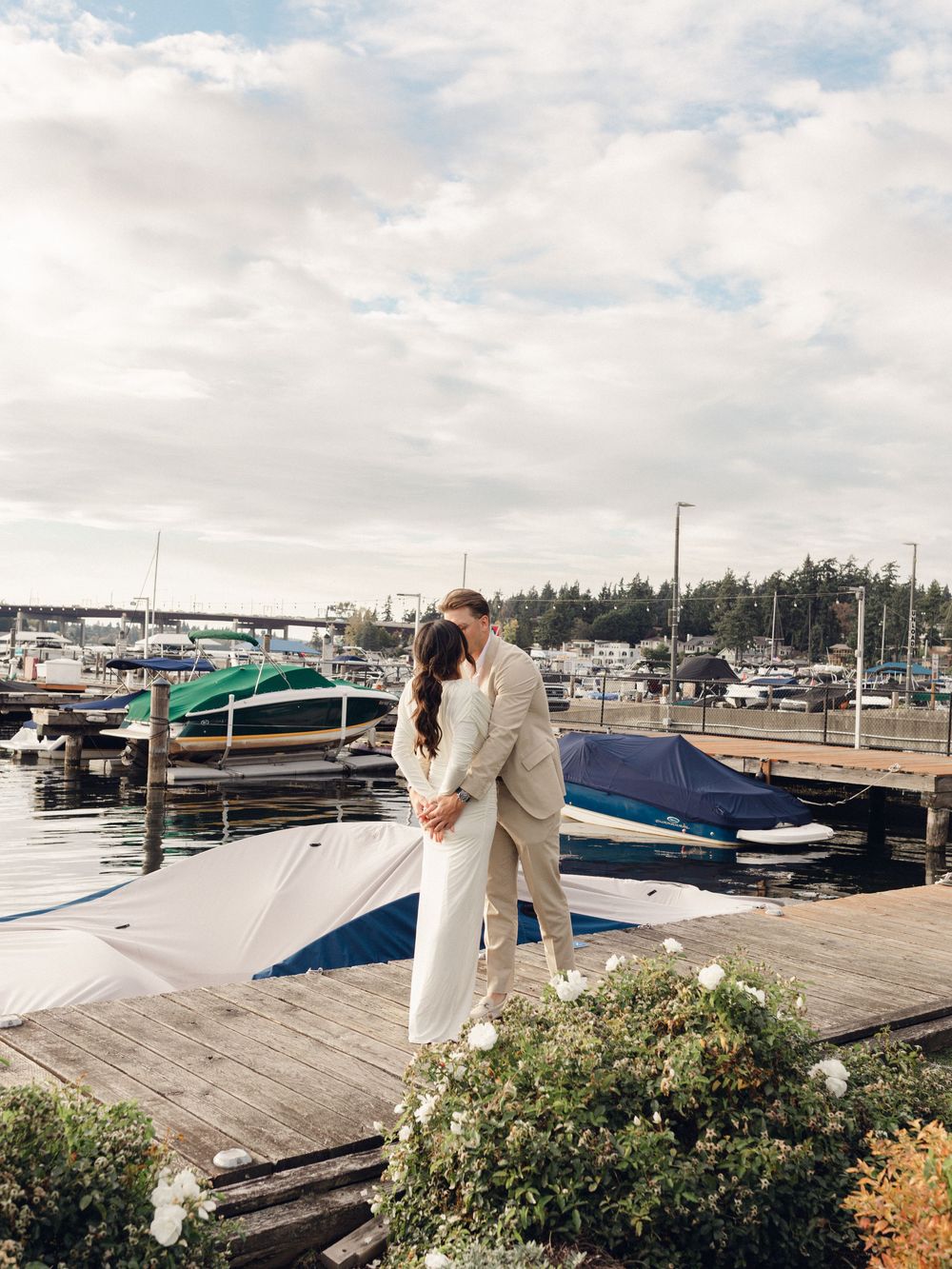 A scenic marina view with docked boats and a couple standing on the wooden pier.