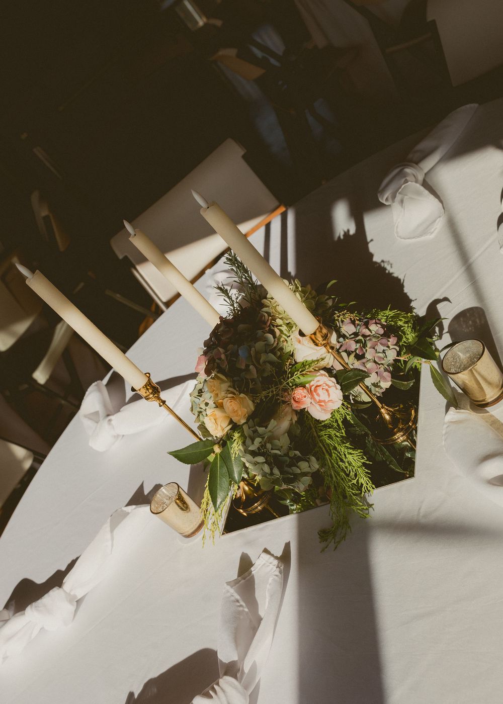 Floral arrangement with roses and greenery casts dramatic shadows on white surface in natural sunlight.