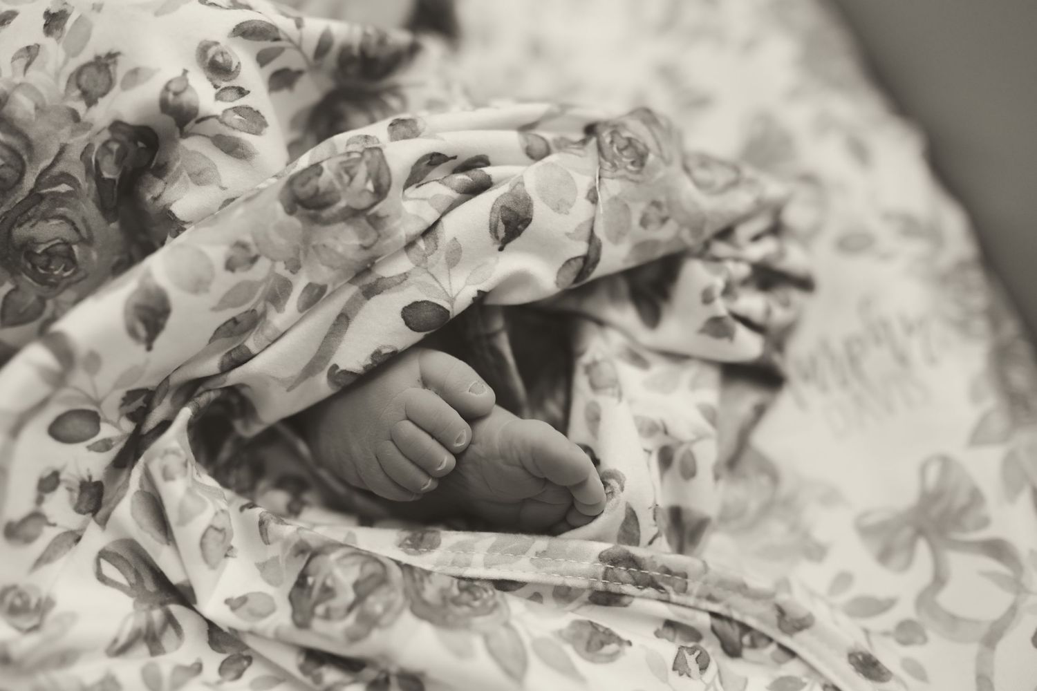 Close-up shots of baby feet touching floral patterned fabric in black and white.