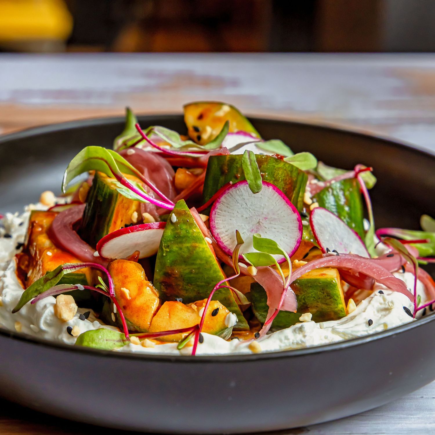 Vibrant salad with roasted vegetables and greens arranged on modern black plates.
