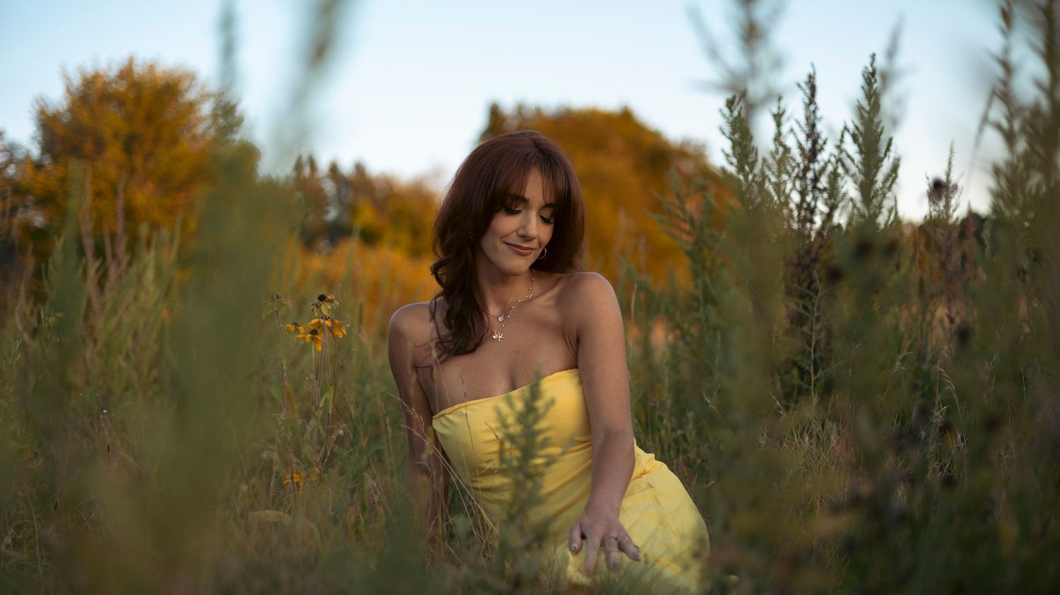 Woman in flowing yellow dress walks through golden field at sunset creating dreamy summer atmosphere.