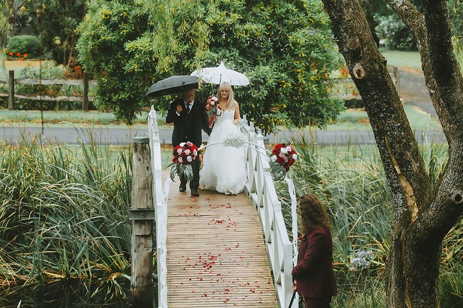 A rustic outdoor wedding ceremony setup with a white arch decorated with floral arrangements in a garden setting.