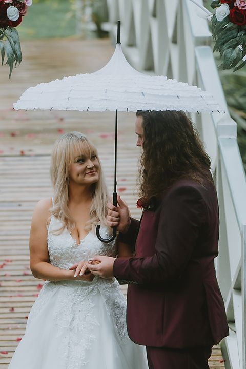 A couple shares a tender moment under a white umbrella during their outdoor wedding ceremony.