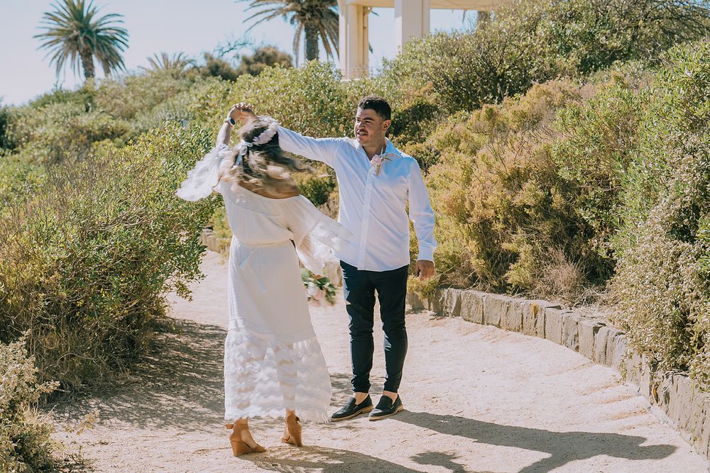 Two people stroll together on a scenic coastal path lined with palm trees and native plants.
