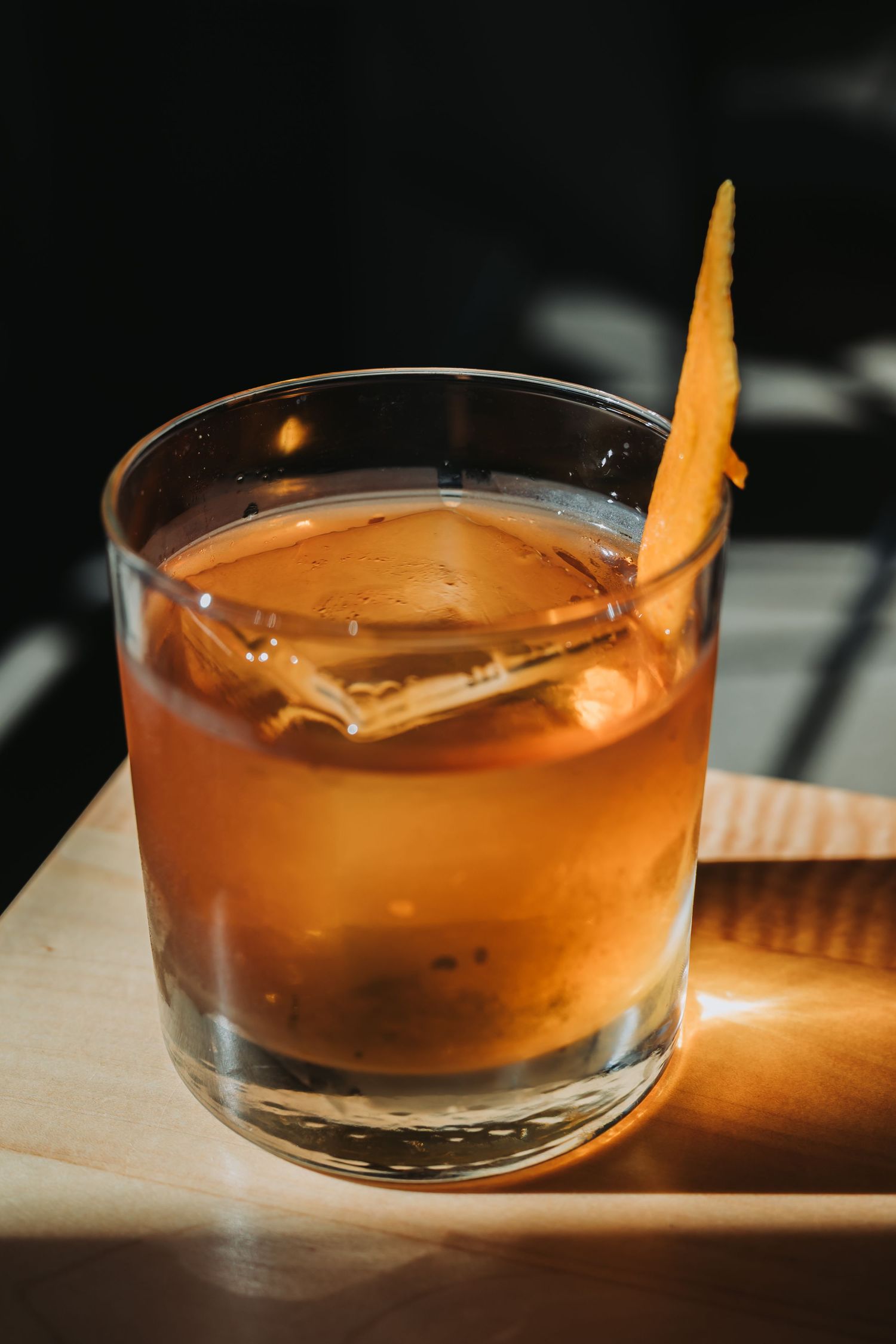 A series of orange cocktails with citrus garnish in lowball glasses photographed from different angles in moody lighting.