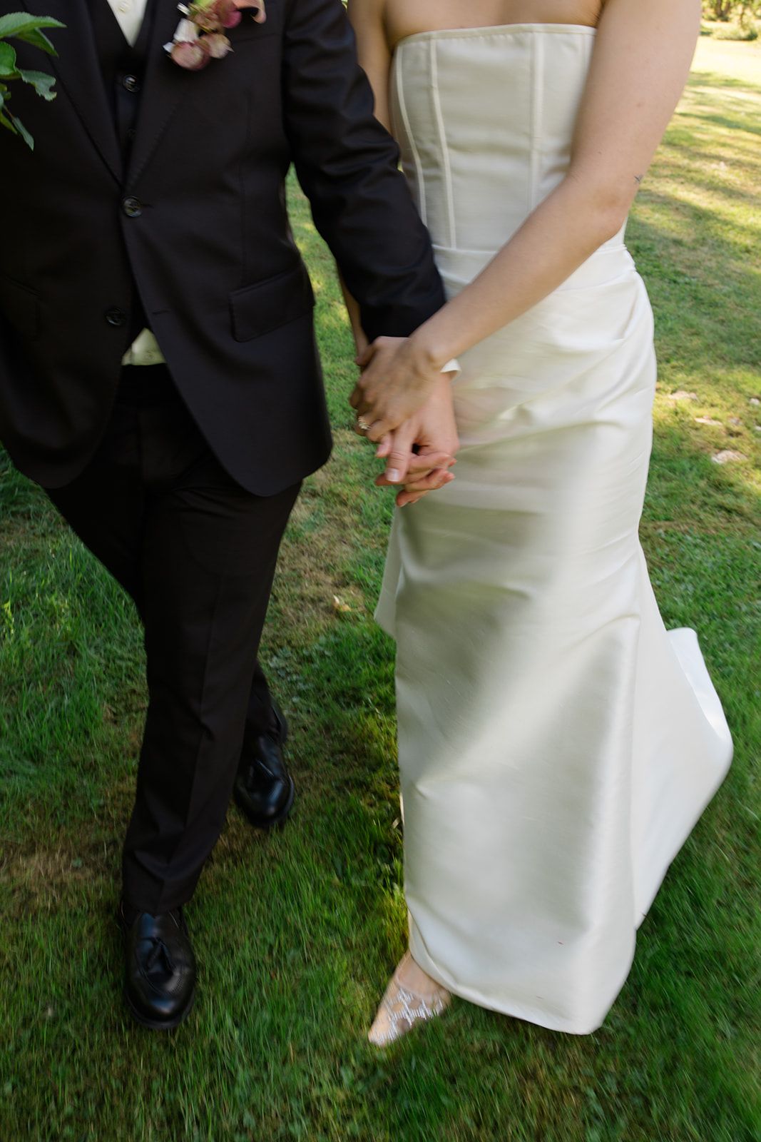 A close-up view of formal wedding attire showing a black tuxedo and white wedding dress against green grass.