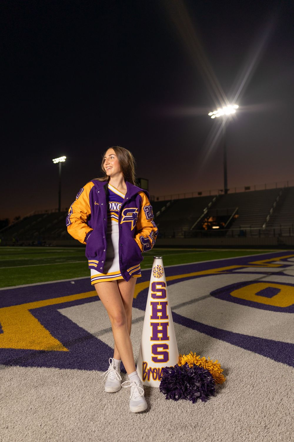 Athletic figure in school colors poses confidently on illuminated sports field at night.