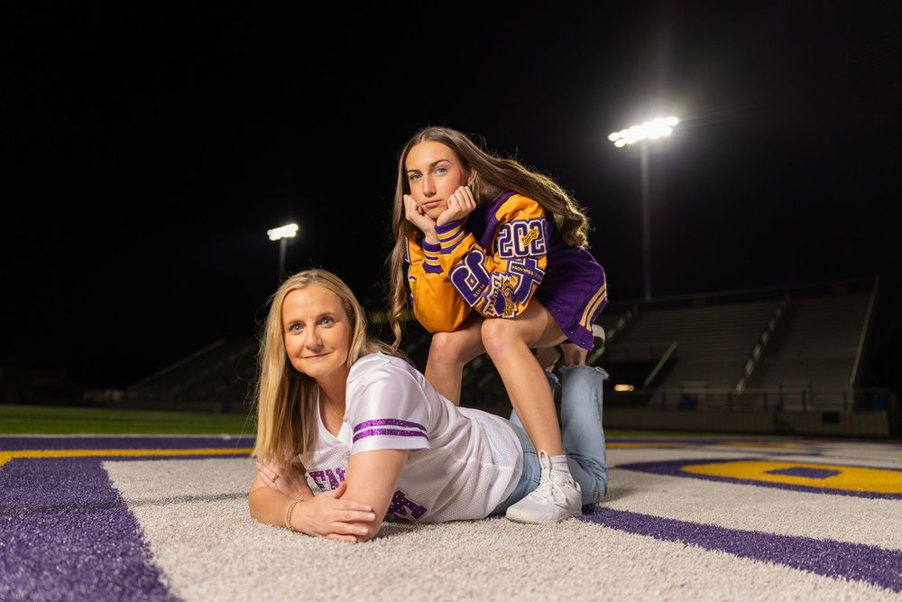 Friends in school athletic wear relaxing on football field during nighttime photoshoot.