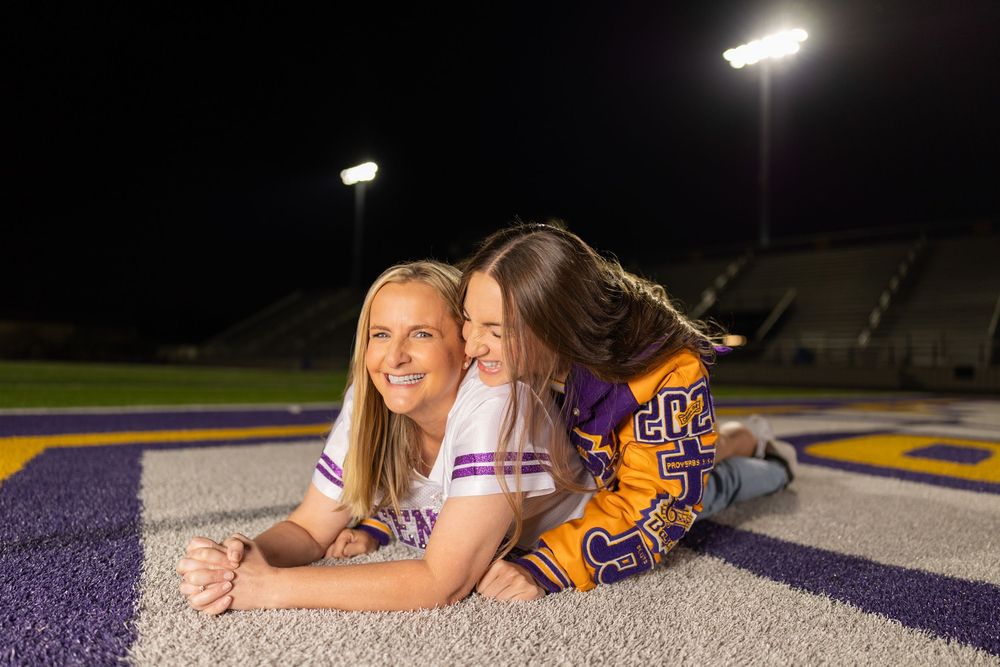 Students in purple and gold uniforms pose casually on illuminated sports field.
