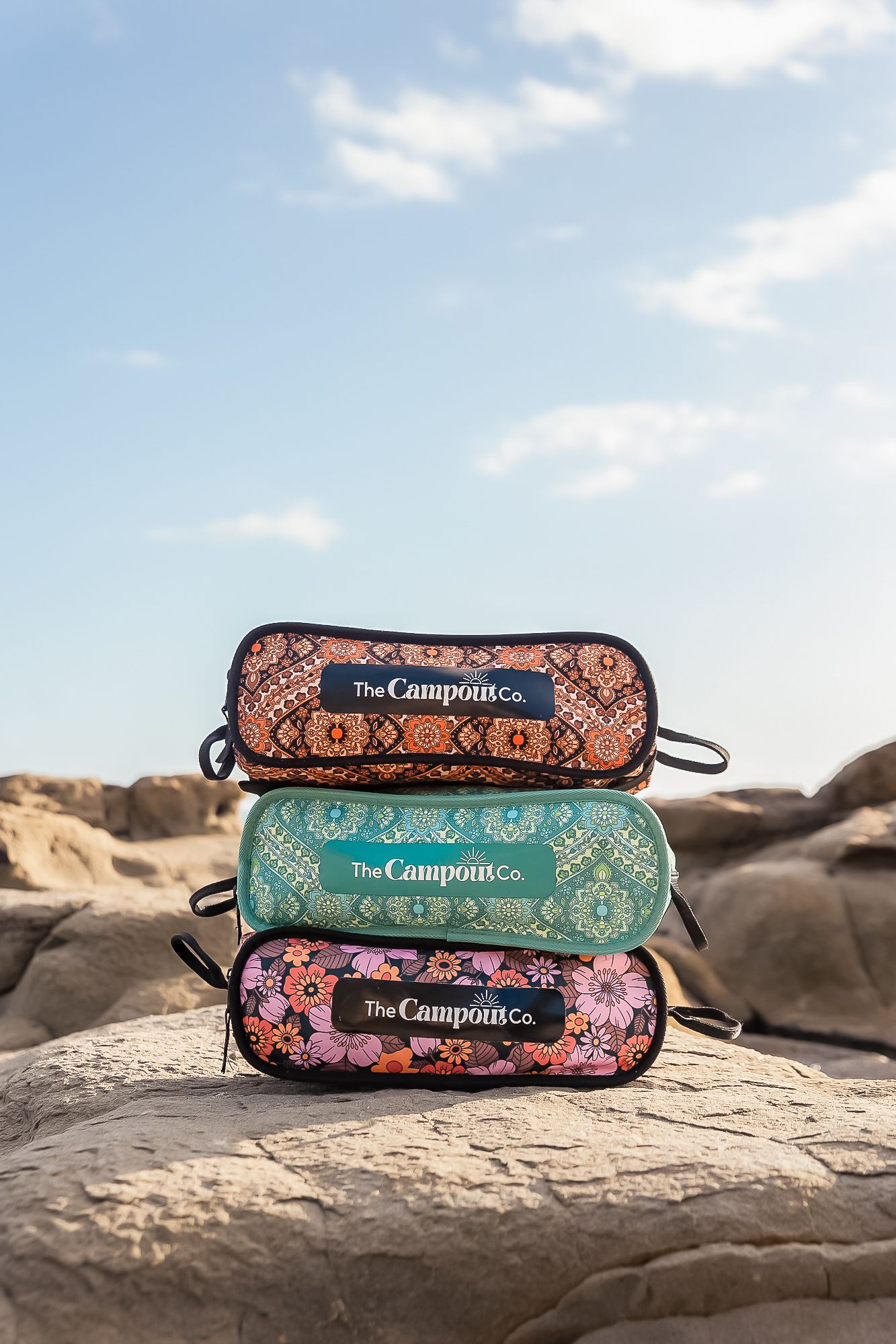 Colorful patterned cosmetic bags from The Camponita Co displayed on rocky terrain.