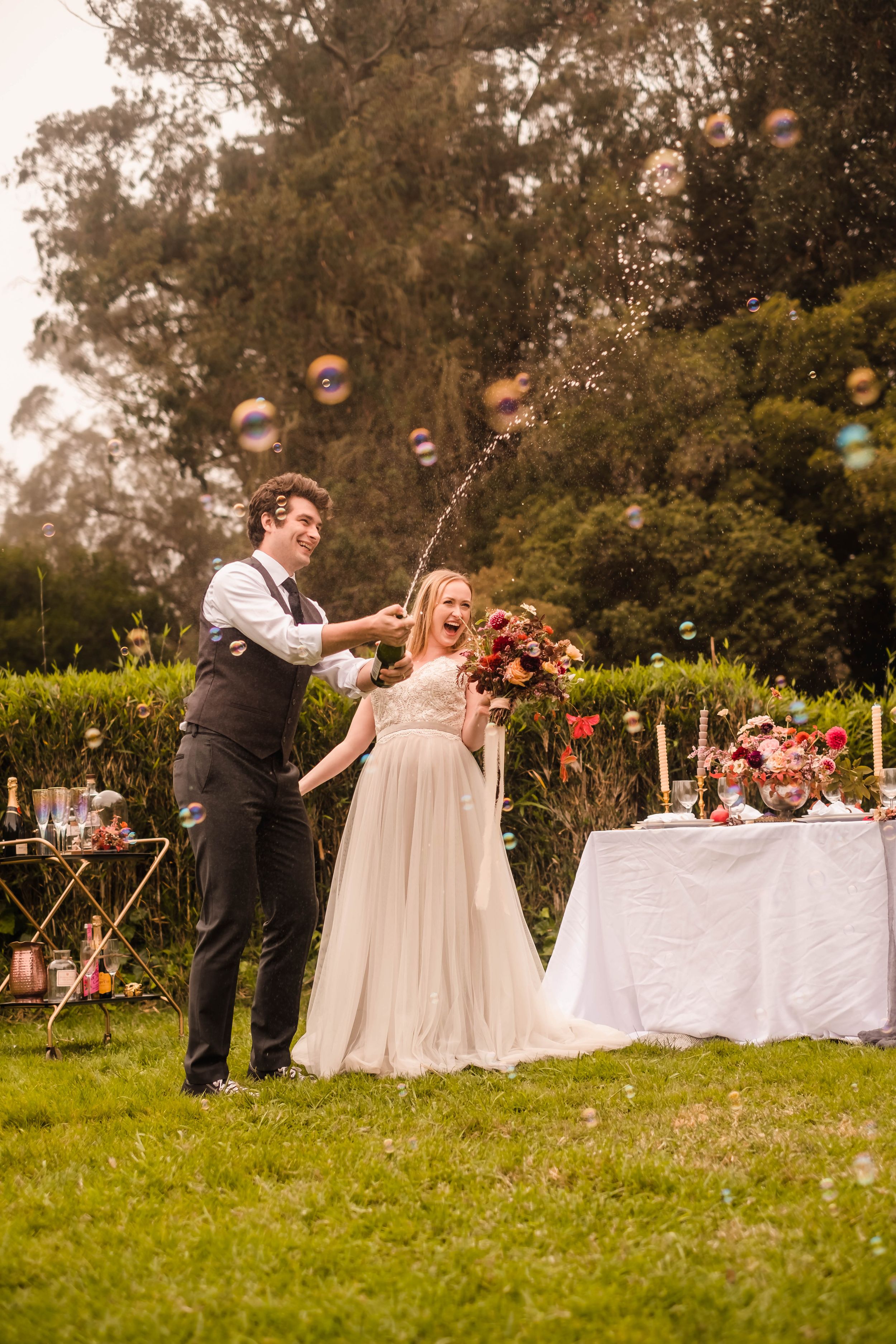 Sarah and Riley popping a bottle of champagne, bubbles floating around them during their Golden Gate Park styled session.