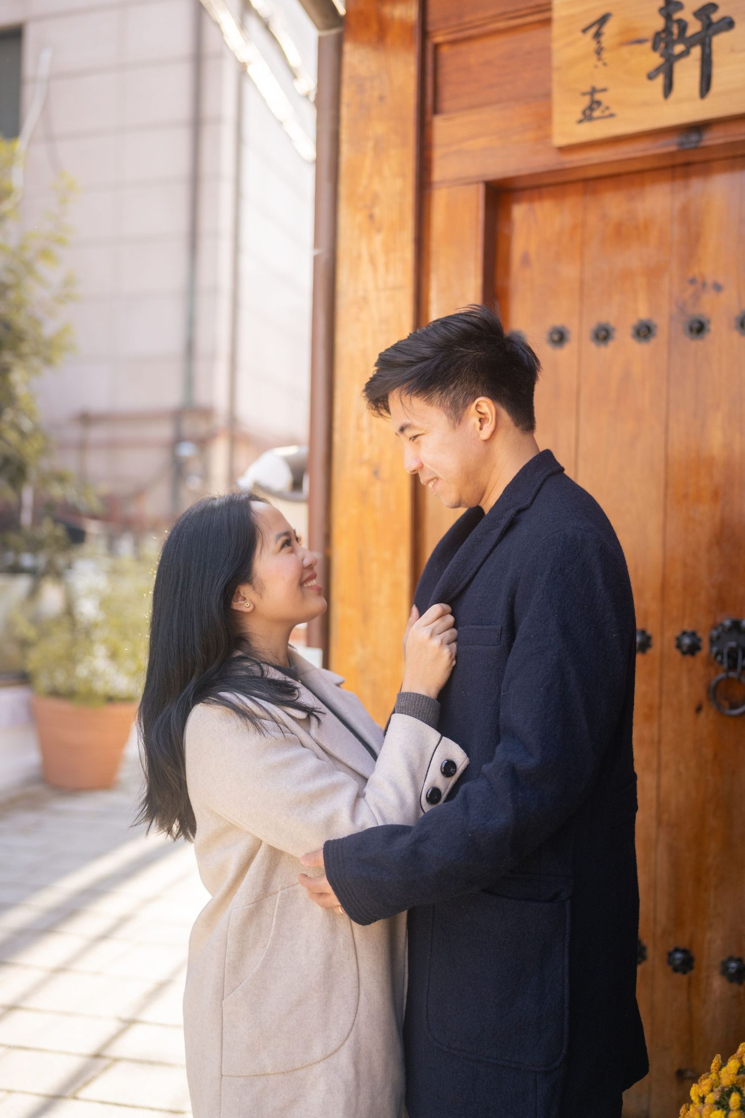A couple shares a playful and romantic moment against a wooden door in traditional Asian architecture.