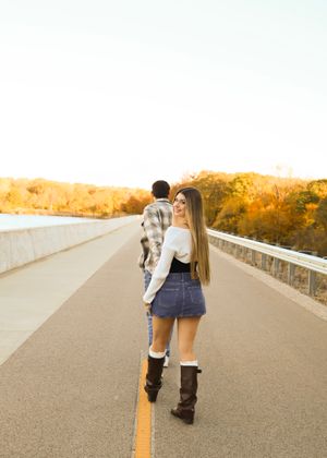 A person carrying a child walks on a bridge during sunset.